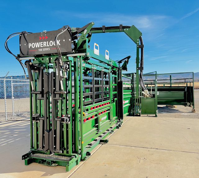 Green mechanical livestock chute under a clear sky.