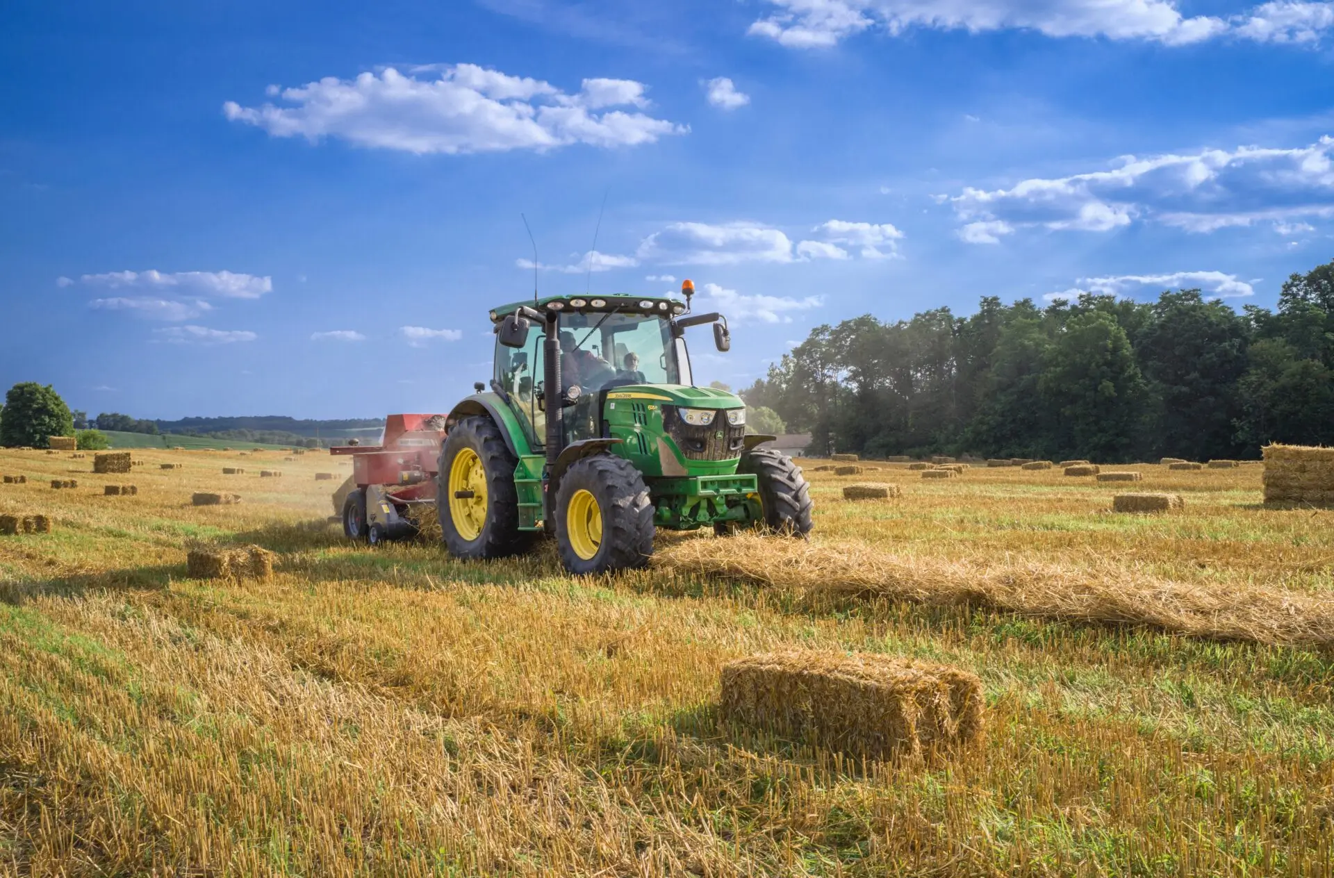 A green tractor baling hay on field.